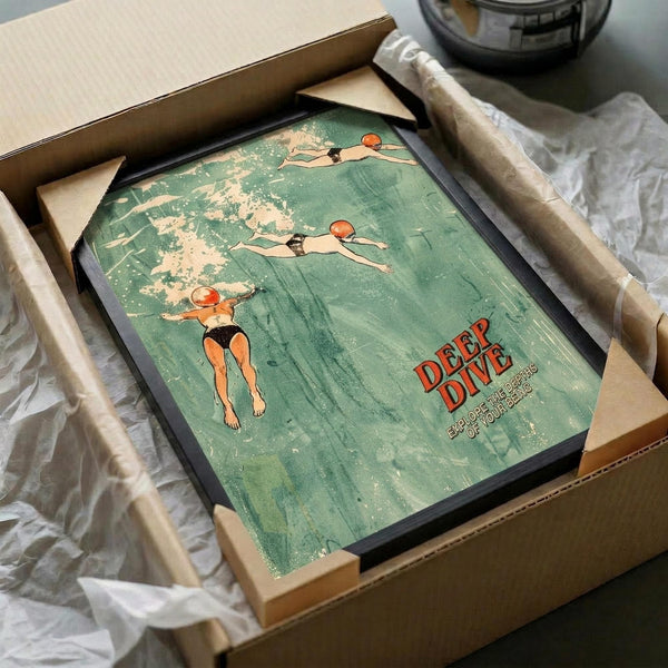 May include: Framed vintage-style poster with aqua green background showing three swimmers diving underwater. The illustration features retro orange and black swimwear with "DEEP DIVE" text in red letters. Black frame sits in cardboard shipping box with white tissue paper padding on white fabric surface.