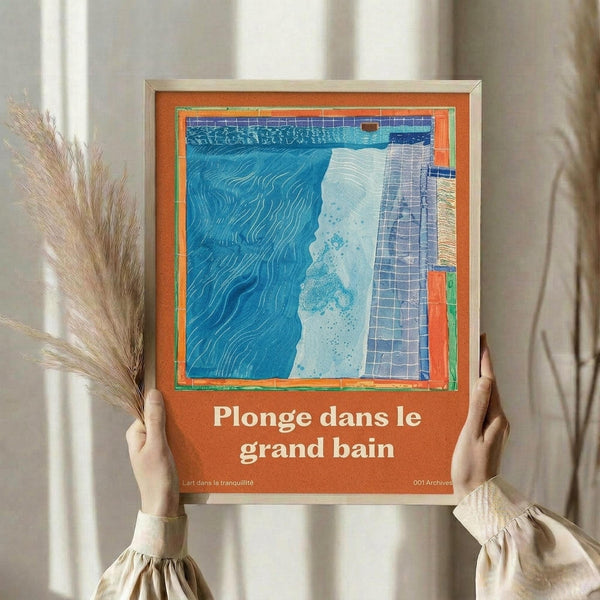 May include: Person holding framed poster with orange border and abstract artwork featuring blue wavy water patterns, white splash areas, and purple grid sections. French text reads "Plonge dans le grand bain" below the colorful swimming pool-inspired design. Dried pampas grass visible beside figure wearing beige ruffled sleeves against neutral curtained background.