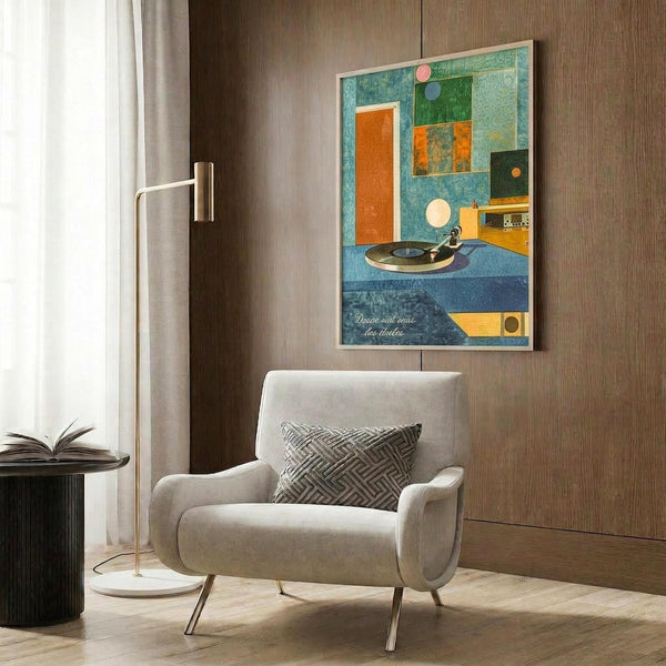 May include: A vintage-inspired poster featuring a geometric composition with colorful blocks in blue, green, orange and cream tones, depicting a turntable and audio equipment with French text at bottom. The framed artwork is displayed on wood-paneled wall above a modern beige armchair with geometric pillow, alongside a brass floor lamp and dark side table with open book.