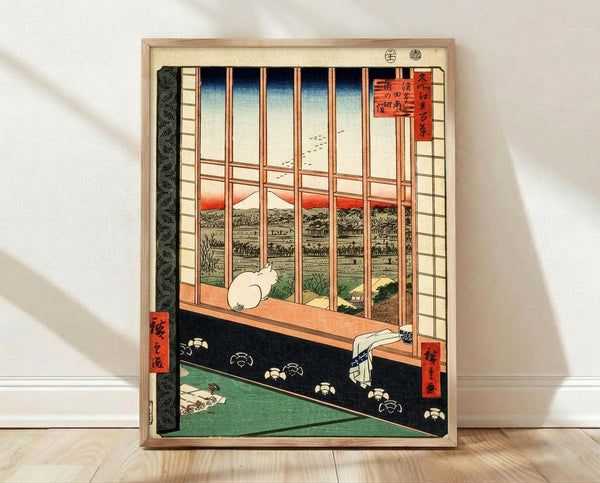 May include: Framed Japanese woodblock print reproduction showing interior view through wooden window grid with white cat sitting on windowsill, overlooking rural landscape with red sunset sky. Print features traditional ukiyo-e style with muted greens, oranges, and blues. Black decorative border with floral pattern on tatami floor. Natural wood frame leaning against white wall on light wooden flooring with soft shadows.