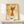 May include: Framed art print featuring an abstract orange cat with pointed ears, yellow eyes, and curved tail on aged paper background, displayed on light wood shelf next to small white gift box with greenery sprig against white wall.