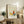May include: Framed art print featuring an abstract butterfly design with yellow, orange, and teal colored wings outlined in black on a cream background. The poster displays "PICASSO" at the top and "Uffizi Gallery Collection de Dessins" at the bottom. The print sits in a light wood frame on a rustic wooden console table alongside books, ceramic vases, and a potted fern plant, creating a warm, minimalist home decor scene with neutral tones throughout.