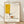 May include: Framed abstract art print in light wood frame leaning against white wall on wooden floor. Artwork features minimalist line drawing of coffee cup with steam on cream background, yellow geometric rectangle, red and green accents. Print shows "PICASSO" at top, "Centre Pompidou" and "Limited Edition Print No. 04/50" at bottom with signature. Soft natural lighting creates diagonal shadows across white textured wall.