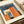 Vintage-style poster featuring geometric architectural forms in orange, blue, and cream colors with "BAUHAUS" text at top and "ARCHITECTURE 1919" at bottom. The design shows overlapping rectangular shapes creating an abstract building composition. Print is displayed on cream paper with rolled paper tubes visible in the background, showing fine texture and matte finish.