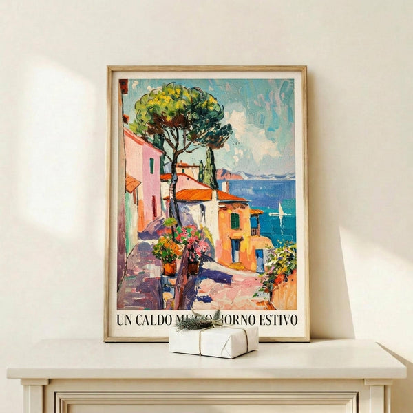 May include: Framed vintage-style travel poster showing colorful Mediterranean coastal village with pink and yellow buildings, large green tree, blue water, and Italian text at bottom. Displayed on light wood shelf with small wrapped gift box beside it against white wall.