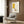 May include: Framed Picasso-style minimalist poster with yellow rectangle, coffee cup, and Centre Pompidou text displayed above beige armchair with geometric pillow in modern living room. Wood-paneled wall, brass floor lamp, and side table with open book create warm, contemporary interior setting.