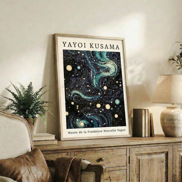 May include: Framed poster with cosmic swirling patterns in deep blues and teals with scattered white and yellow dots, displayed on rustic wood sideboard. Room scene shows neutral armchair, potted fern, ceramic vessels, and books creating cozy living space with cream walls and warm natural lighting.