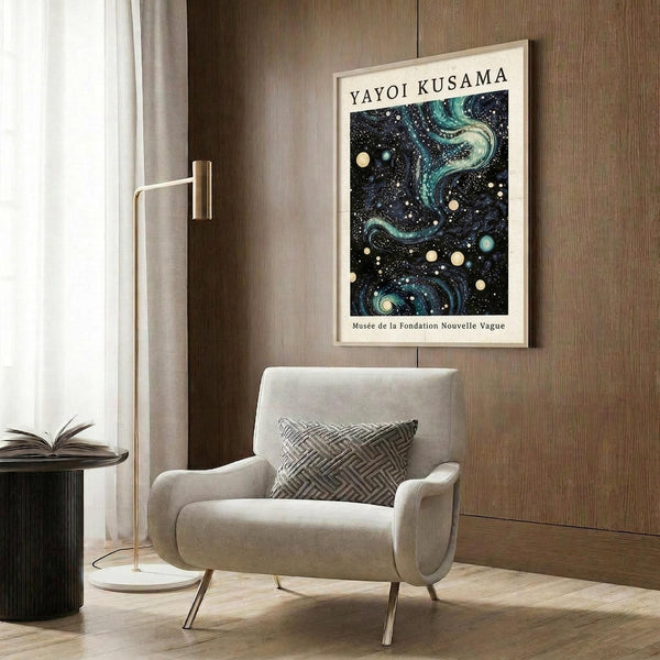 May include: Framed art poster with cosmic design featuring swirling blue and green patterns, white dots and circles on dark background, displayed above modern cream armchair with geometric pillow. Room has wood panel walls, brass floor lamp, and dark round side table with open book.