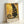 A framed art print featuring a black cat in the ornate golden style of Gustav Klimt, with intricate circular patterns, geometric designs, and rich amber and gold tones throughout. The cat sits regally against a decorative background filled with spirals, dots, and mosaic-like elements. Text at the bottom reads "NINE LIVES OF LUXURY" and "NO PAWS IN MY PLANS, ONLY PURRFECTION." The wooden frame leans against a white wall.