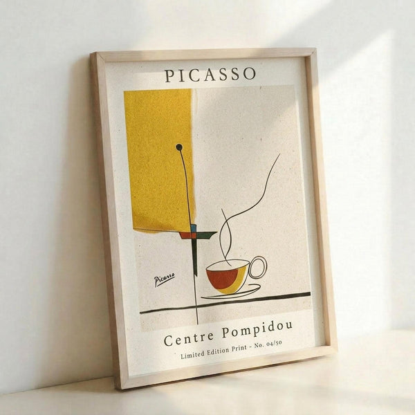 May include: A framed poster print featuring abstract geometric shapes in mustard yellow and earth tones with a stylized coffee cup, displayed in a light wood frame against a white wall. The minimalist artwork shows clean lines and modern artistic elements with text reading "PICASSO" at top and "Centre Pompidou" at bottom, indicating it's a limited edition print numbered 04/50.