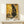 May include: Framed poster featuring a black cat in Gustav Klimt's ornate golden style with geometric patterns, circular motifs, and rich yellow background. The artwork shows intricate decorative elements and swirling designs characteristic of Art Nouveau. Small white gift box sits on light wood shelf below the natural wood-framed print against white wall.