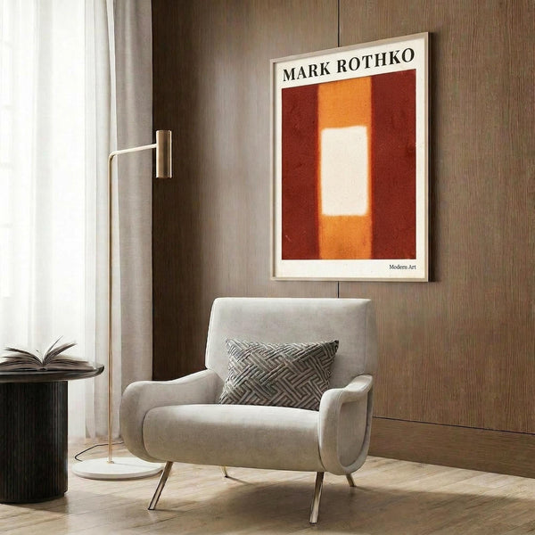 May include: Abstract color field artwork poster with orange, red, and white rectangular forms hanging on wood-paneled wall above beige upholstered armchair with geometric patterned pillow. Modern brass floor lamp and round black side table with open book complete the sophisticated living room setting with warm neutral tones and contemporary furnishings.