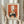 May include: Person holding framed vintage-style poster featuring orange and cream illustration of cats around black table with green vase and flowering branches, displayed in neutral room setting with dried pampas grass and soft natural lighting