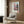 May include: Japanese-style poster print featuring cherry blossoms and traditional pagoda temple in pink, blue and green tones, displayed in light wood frame on dark wood paneled wall above beige upholstered armchair with geometric patterned pillow, brass floor lamp and small round table with open book nearby