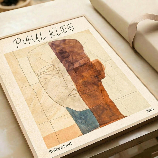 May include: Paul Klee abstract artwork print from 1924 displayed on cream-colored paper in an open book or portfolio, alongside rolled white papers and beige ribbon. The modernist composition features geometric shapes in warm browns, oranges, and blue-green tones with linear sketched elements against a neutral background.