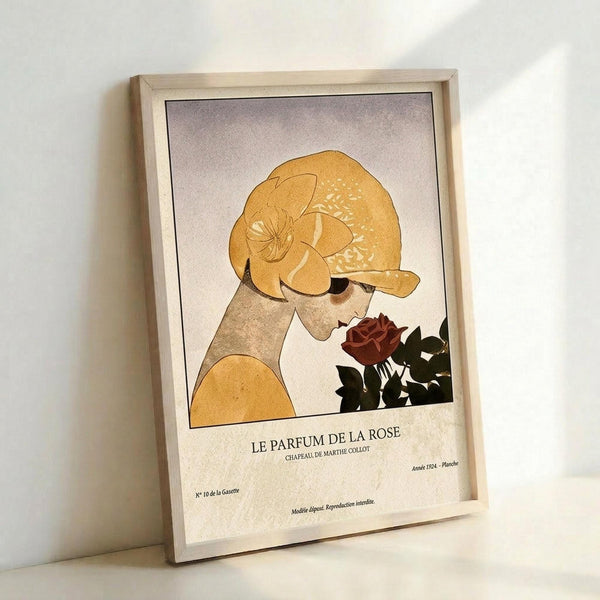 May include: Framed vintage-style art print leaning against white wall showing woman in golden yellow cloche hat smelling red rose, with French text "Le Parfum de la Rose" below illustration. Light wood frame, cream background with subtle texture, warm lighting casting soft shadows.