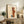 May include: Framed Paul Klee abstract art print displayed on rustic wooden sideboard in warm, neutral-toned living room. The artwork features geometric shapes in orange, brown, and blue tones with linear elements. Scene includes fern plant, ceramic vase, stacked books, and beige upholstered chair, creating a cozy modern home interior setting.