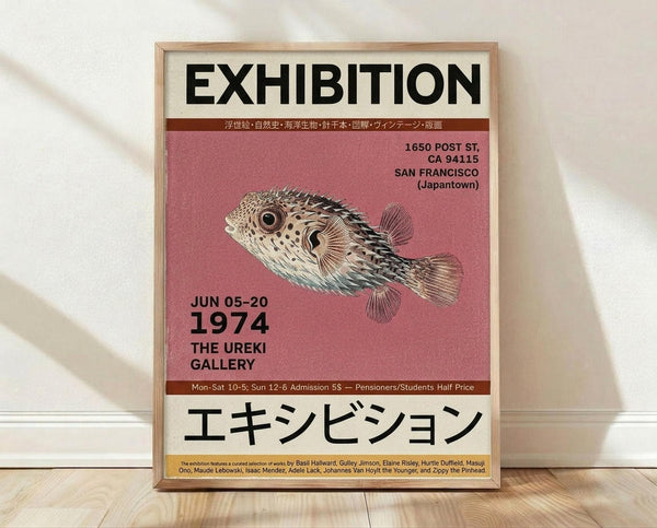 May include: Framed exhibition poster with beige background featuring detailed illustration of pufferfish on coral pink section. Black text shows "EXHIBITION" at top, dates "JUN 05-20 1974", San Francisco Japantown address, and Japanese characters at bottom. Japanese text and artist names listed. Natural wood frame leaning against white wall on light wooden floor with soft shadows.