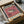 May include: Vintage-style exhibition poster featuring a detailed pufferfish illustration on coral pink background, displayed in black frame inside cardboard shipping box with protective tissue paper and wooden dowels for packaging.