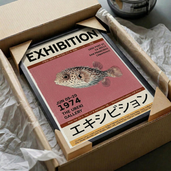 May include: Vintage-style exhibition poster featuring a detailed pufferfish illustration on coral pink background, displayed in black frame inside cardboard shipping box with protective tissue paper and wooden dowels for packaging.