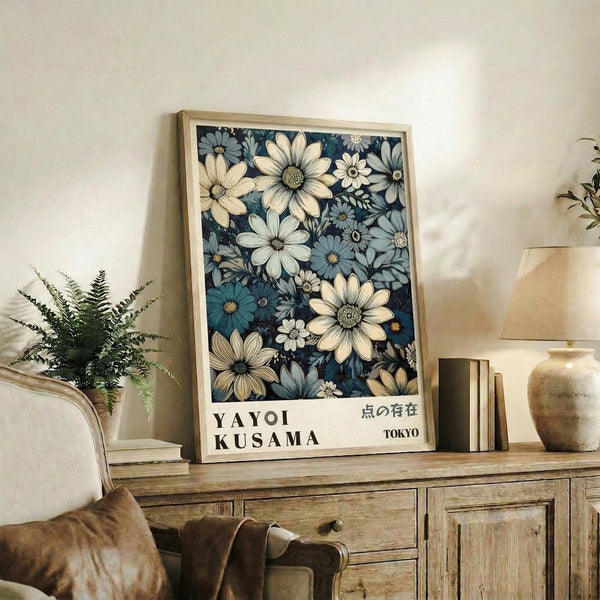 May include: Framed floral art print with white and blue cosmos flowers on dark navy background, displayed on rustic wooden sideboard next to fern plant, ceramic vase, and books in neutral-toned living room setting with beige upholstered furniture.