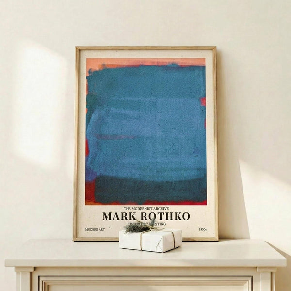May include: Framed abstract art print with horizontal bands of blue watercolor paint and orange-red accents at edges, displayed on light wood shelf against white wall. Small wrapped gift box sits in front of the natural wood frame. The artwork features soft, blended brushstrokes in various blue tones creating layered rectangular forms typical of color field painting style.