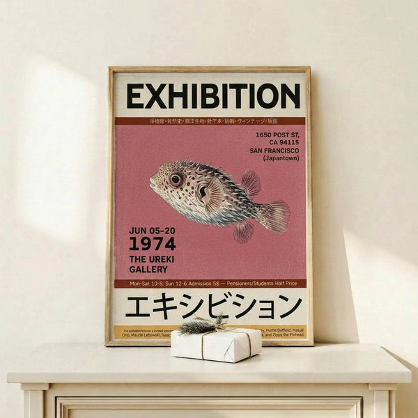 May include: Framed exhibition poster with pink background featuring detailed pufferfish illustration, displayed on light wood shelf against cream wall. Poster shows Japanese and English text including "1974" and "The Ureki Gallery" with San Francisco Japantown address. Small wrapped gift box with twine sits in front of thin gold frame.