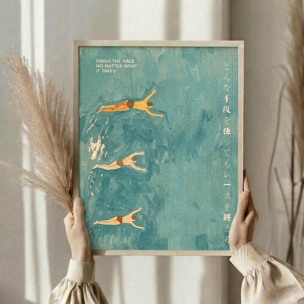May include: Hands holding a framed art print showing three swimmers diving through turquoise blue water with Japanese text on the right side and "FINISH THE RACE NO MATTER WHAT IT TAKES" at the top. Natural wood frame against white curtained window with dried pampas grass stems visible on the left side.
