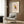 May include: Framed poster featuring a geometric owl in Picasso's minimalist style with colorful angular shapes in yellow, blue, orange and red against a pink background. The print hangs on wood-paneled wall above a cream upholstered armchair with patterned pillow. Modern reading nook includes brass floor lamp and side table with open book.