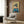 May include: Japanese art print featuring a geisha in blue kimono with red collar against golden cherry blossom background, displayed on wood-paneled wall above modern beige armchair with geometric pillow, brass floor lamp and side table visible in contemporary room setting.