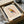 May include: Framed minimalist owl print in geometric style with red, yellow, and blue triangular shapes on cream background, packaged in brown cardboard box with protective tissue paper, displayed on white fabric surface alongside wooden tubes and glass object