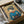 May include: Framed Japanese-style artwork showing a geisha in blue kimono with red collar holding an umbrella, surrounded by cherry blossom branches on golden background. Print displayed in dark frame inside cardboard shipping box with protective tissue paper wrapping.