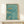 May include: Framed poster with turquoise blue watercolor background showing three swimmers diving or swimming, with English text "FINISH THE RACE NO MATTER WHAT IT TAKES" and vertical Japanese characters on the right side. Thin wooden frame sits on white wooden shelf against cream wall with natural lighting casting soft shadows.