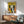 May include: Colorful cat illustration poster with yellow background showing various stylized felines in black, orange, gray, and white. Mid-century modern living room setting with wooden credenza, sage green upholstered chair with wood arms, white ceramic table lamp, and natural sunlight casting geometric shadows on white walls.
