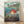 May include: Framed Studio Ghibli Ponyo movie poster print leaning against white textured wall on light wood floor. Features red-haired Ponyo character swimming in ocean water with coastal village in background. Japanese and English text visible. Natural wood frame with glass. Soft natural lighting creates gentle shadows on wall.