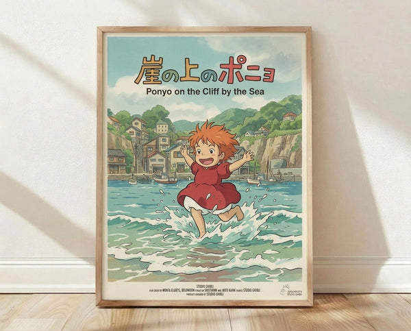 May include: Framed Studio Ghibli Ponyo poster showing red-haired child character splashing joyfully in turquoise ocean waves with arms raised, coastal town and green hills in background, Japanese and English text at top, light wood frame leaning against white textured wall on wooden floor with soft natural lighting and shadows
