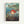 A framed Studio Ghibli movie poster for Ponyo on the Cliff by the Sea, featuring the red-haired character Ponyo swimming in turbulent ocean water near rocky cliffs. The artwork shows a coastal town with green hills in the background under a cloudy sky. Japanese text appears at the top and bottom along with the English title. The poster has Studio Ghibli's distinctive hand-drawn animation style with vibrant blues, greens, and the character's bright red hair as focal points. Light wood frame again