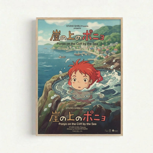 A framed Studio Ghibli movie poster for Ponyo on the Cliff by the Sea, featuring the red-haired character Ponyo swimming in turbulent ocean water near rocky cliffs. The artwork shows a coastal town with green hills in the background under a cloudy sky. Japanese text appears at the top and bottom along with the English title. The poster has Studio Ghibli's distinctive hand-drawn animation style with vibrant blues, greens, and the character's bright red hair as focal points. Light wood frame again
