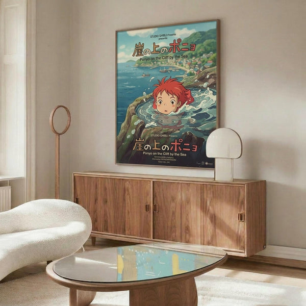 May include: Framed Studio Ghibli Ponyo poster displayed above a mid-century modern walnut credenza in a minimalist living room. The colorful anime artwork shows red-haired Ponyo swimming in ocean water with Japanese text. White modern chair, glass coffee table, and table lamp visible. Warm natural lighting creates shadows on cream walls.