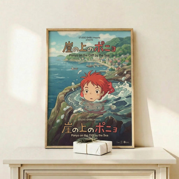 May include: Framed Studio Ghibli Ponyo movie poster displayed on light wood shelf against white wall. Features red-haired boy character swimming in ocean waves with coastal town backdrop. Japanese and English text visible. Small white wrapped gift with green sprig sits nearby. Warm natural lighting creates soft shadows.