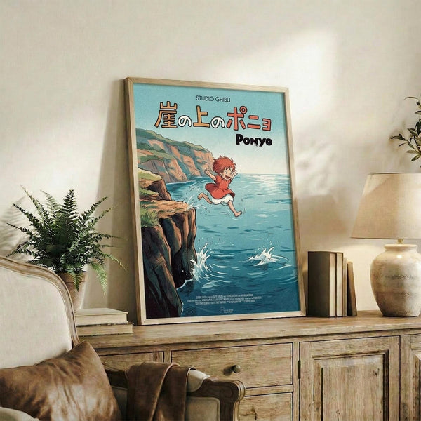 May include: Framed Studio Ghibli Ponyo poster displayed on rustic wooden sideboard in cozy living room setting. Poster shows red-haired boy jumping off coastal cliff into blue ocean water with Japanese text above. Natural wood frame, surrounded by fern plant, ceramic vase, stacked books, and cream upholstered chair with brown leather pillow.