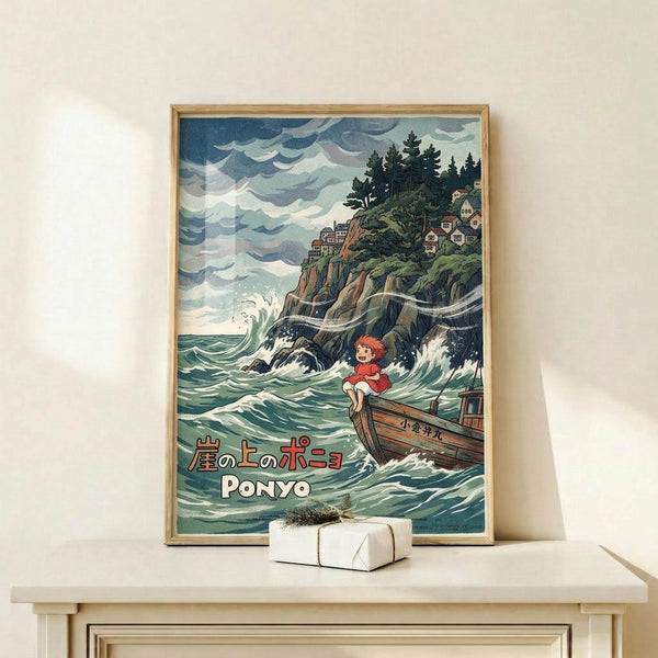 May include: Framed Studio Ghibli Ponyo poster displayed on light wood console against white wall. Artwork shows red-haired child character on wooden boat amid churning green-blue ocean waves, with dramatic cloudy sky and clifftop houses with evergreen trees in background. Japanese and English text at bottom. Small white wrapped gift box sits on console surface next to frame.