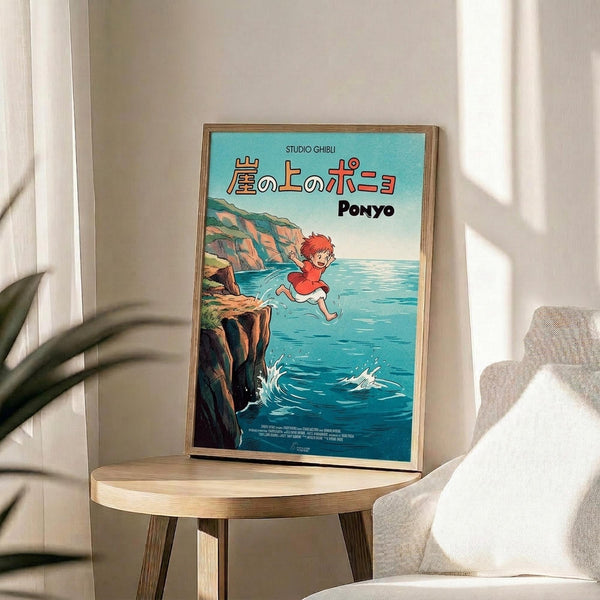 May include: Framed Studio Ghibli Ponyo movie poster displayed on round wooden side table next to beige upholstered chair. Poster shows red-haired child character jumping over turquoise ocean water near rocky coastal cliffs under blue sky. Japanese text and "PONYO" title visible at top. Natural lighting creates soft shadows on white wall behind. Green plant leaves partially visible in corner.
