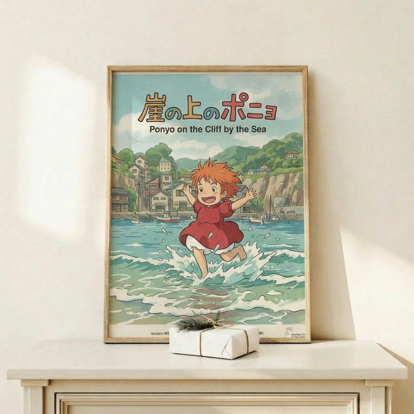 May include: Framed Studio Ghibli Ponyo poster displayed on light wood shelf against cream wall. Artwork shows red-haired child in red dress running through ocean waves with Japanese coastal town in background. Soft pastel colors in anime illustration style. Natural wood frame, small white gift box with twine bow sits in front of poster.
