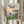 May include: Person holding framed Ponyo movie poster in light wooden frame against white curtained window, with dried pampas grass stems. Poster shows red-haired girl in red dress overlooking coastal village with boats, mountains, and sunset sky. Japanese text and "PONYO" title visible. Vintage-style anime artwork with soft pastels and detailed landscape illustration.