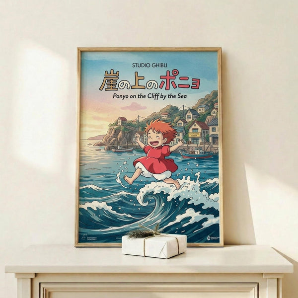 May include: Framed Studio Ghibli Ponyo movie poster displayed on light wood shelf against cream wall. Poster shows red-haired girl character jumping above ocean waves with coastal village in background, rendered in colorful anime art style. Small white wrapped gift box sits on shelf beside the wooden-framed print.
