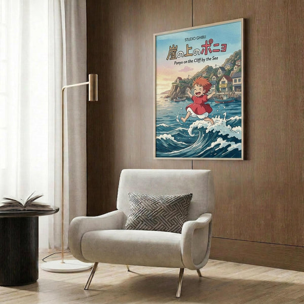 May include: Framed Studio Ghibli Ponyo movie poster mounted on wood-paneled wall above beige upholstered armchair. Poster shows red-haired girl character running through blue ocean waves with coastal village in background. Modern living room setting with brass floor lamp, geometric throw pillow, and open book on dark side table.