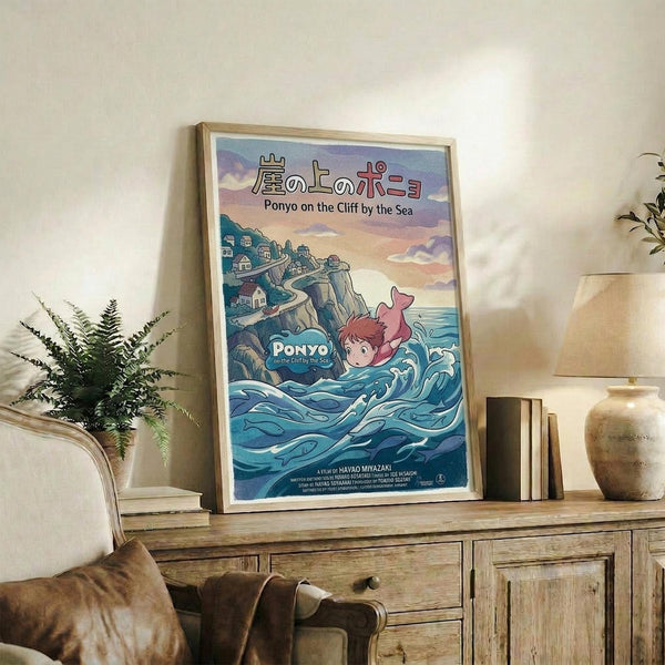 May include: Framed Studio Ghibli Ponyo movie poster displayed on rustic wooden console table beside fern plant, books, and ceramic vase. Poster shows red-haired boy swimming in blue ocean waves near clifftop village with Japanese and English text. Warm natural lighting illuminates cozy living room setting with beige armchair.