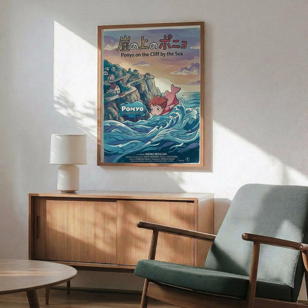 May include: Studio Ghibli-style movie poster in wooden frame hanging above mid-century modern furniture. Features animated character with red hair swimming in turquoise ocean waves near clifftop village. Japanese and English text visible. Poster displayed in minimalist room with sage green armchair, wooden credenza, white table lamp, and natural sunlight casting shadows on white walls.