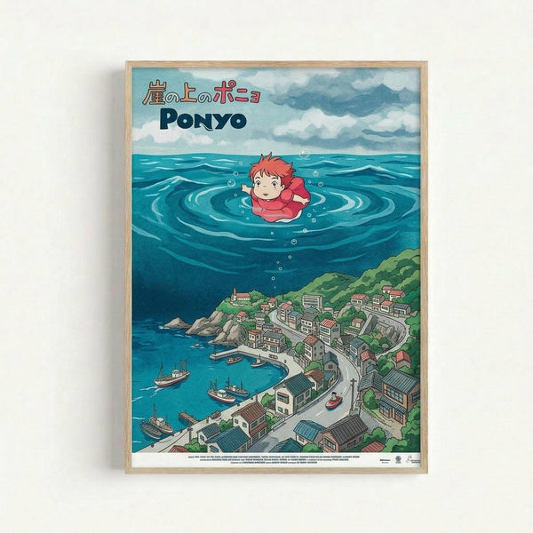 Framed poster featuring Studio Ghibli's Ponyo anime artwork with Japanese and English text at top. Shows red-haired child character Ponyo floating in ocean water above a detailed coastal Japanese village with traditional houses, boats in harbor, and winding roads. Art style is colorful hand-drawn animation with blue ocean, cloudy sky, and green hillside town below. Natural wood frame against white wall.